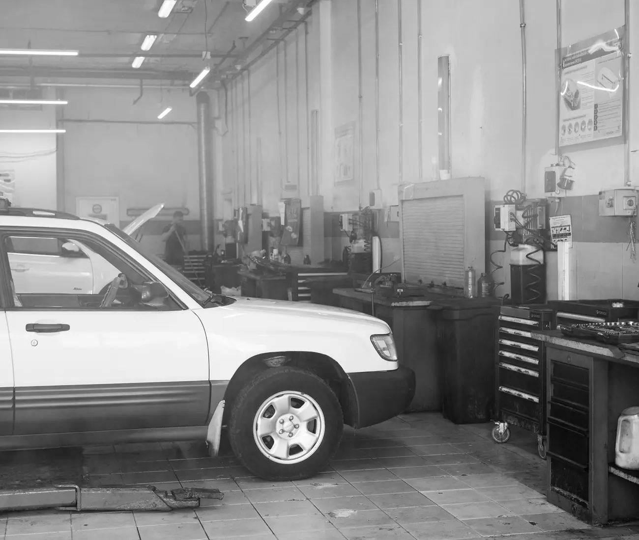 A car in a workshop bay surrounded by tool chests, in black and white