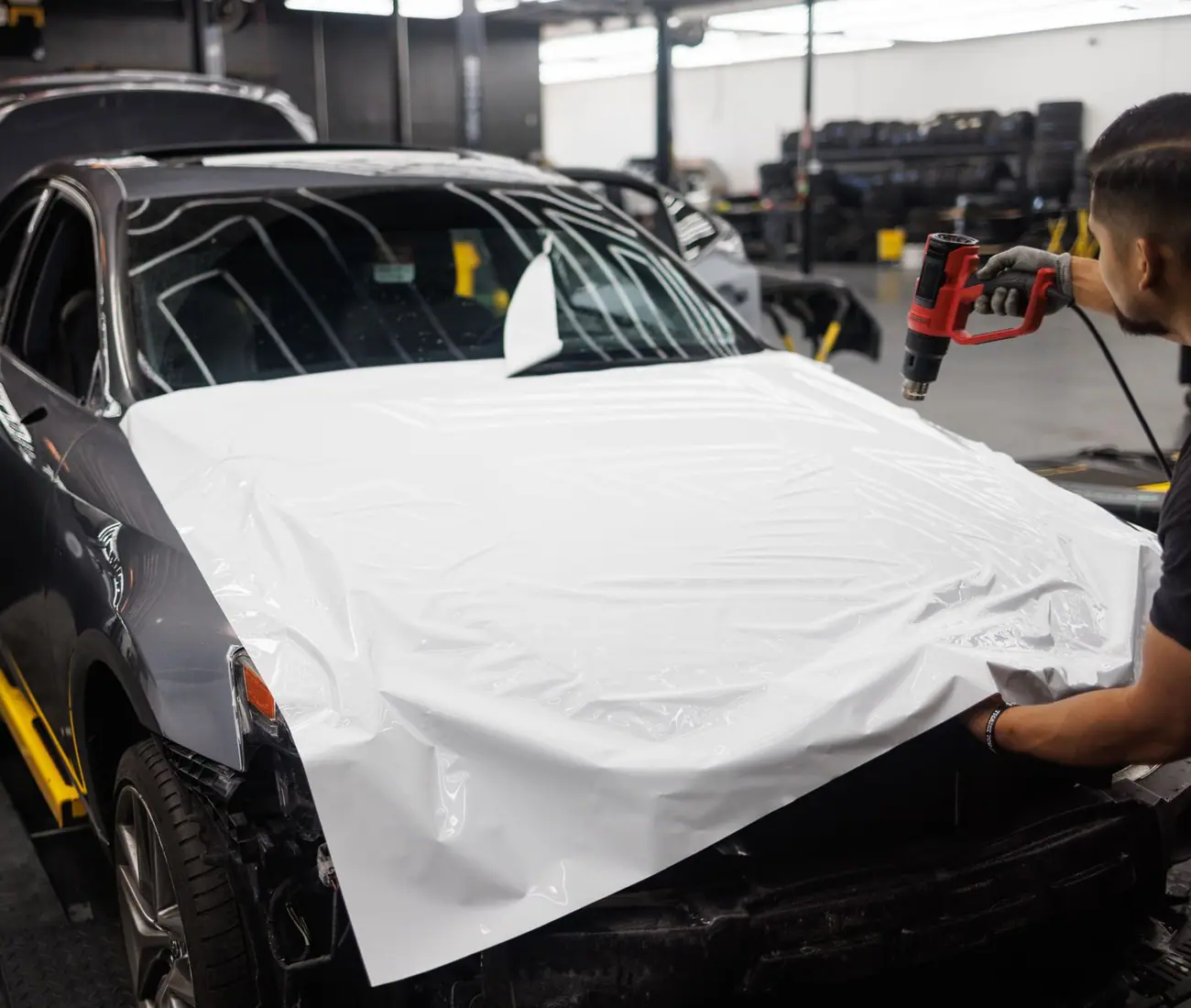 A car covered in white film in a workshop, mid install