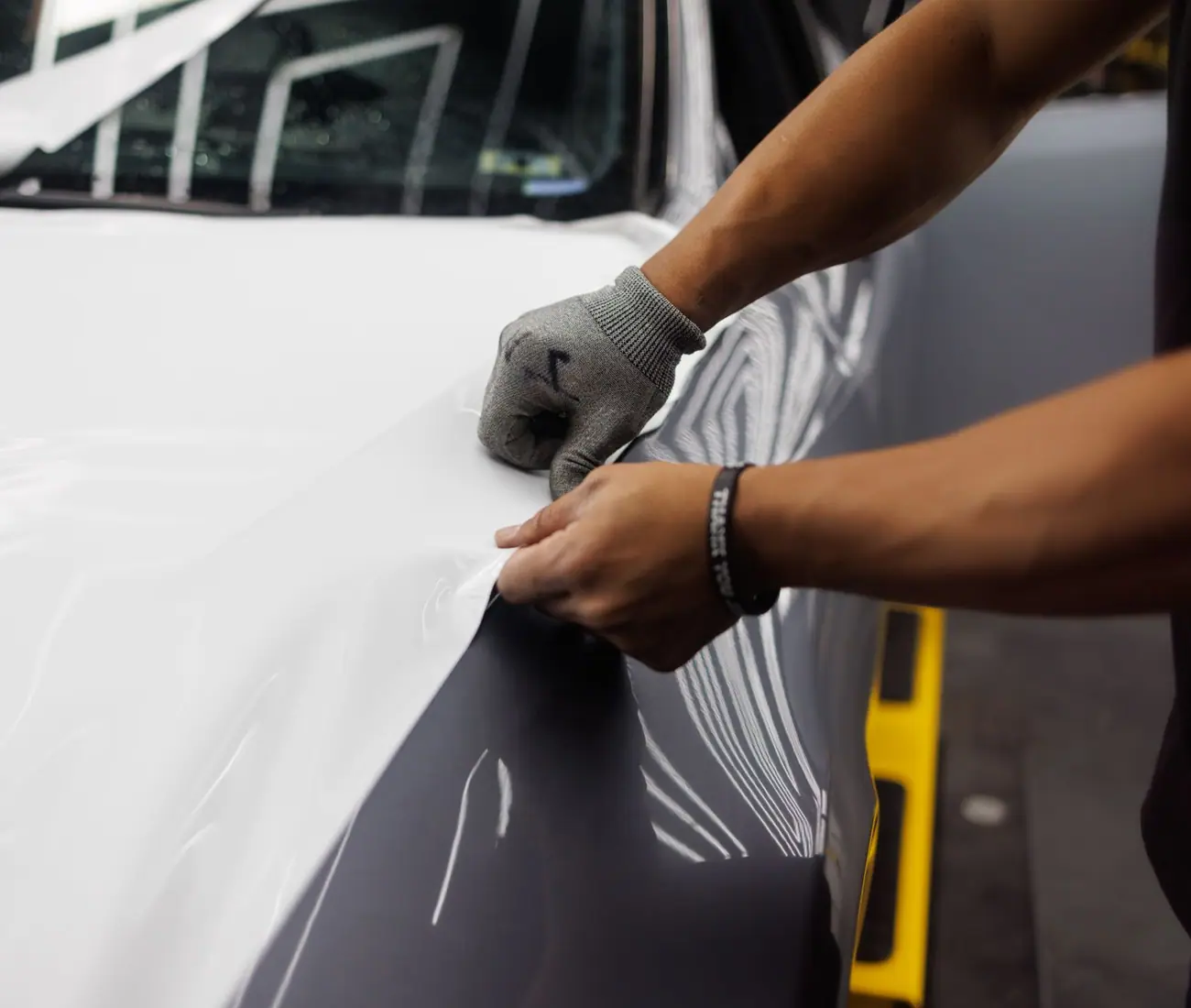 Gloved hands working a squeegee across white film on a panel