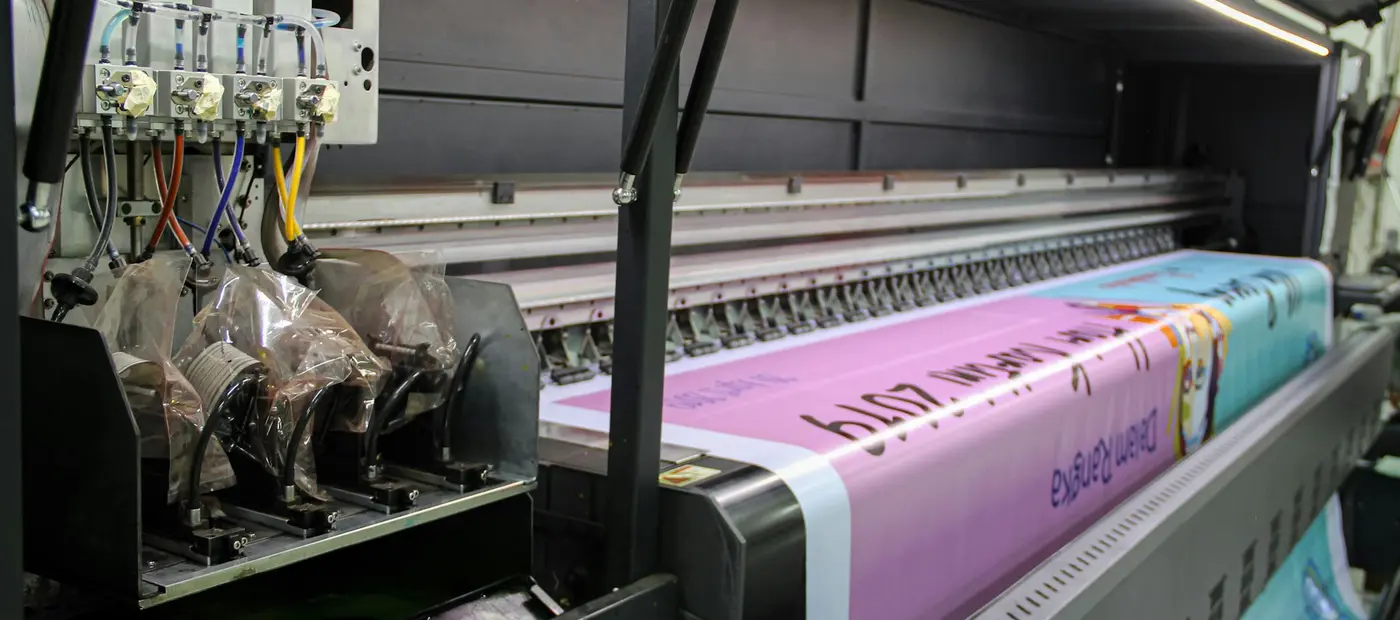 A wide-format press running a full-colour print out onto a roll, ink heads tracking across the material