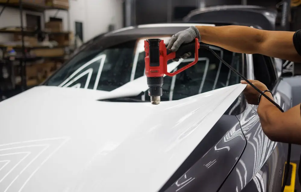 A heat gun worked across freshly laid film on a vehicle panel, setting the material into its shape