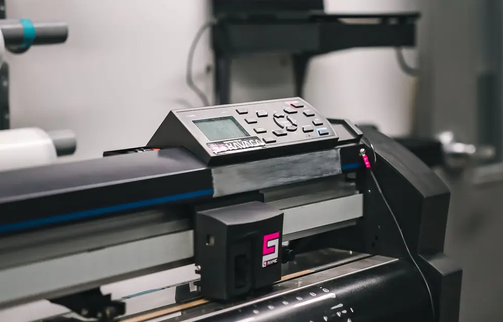 A wide-format printer in a print room, material loaded and the carriage tracking across it